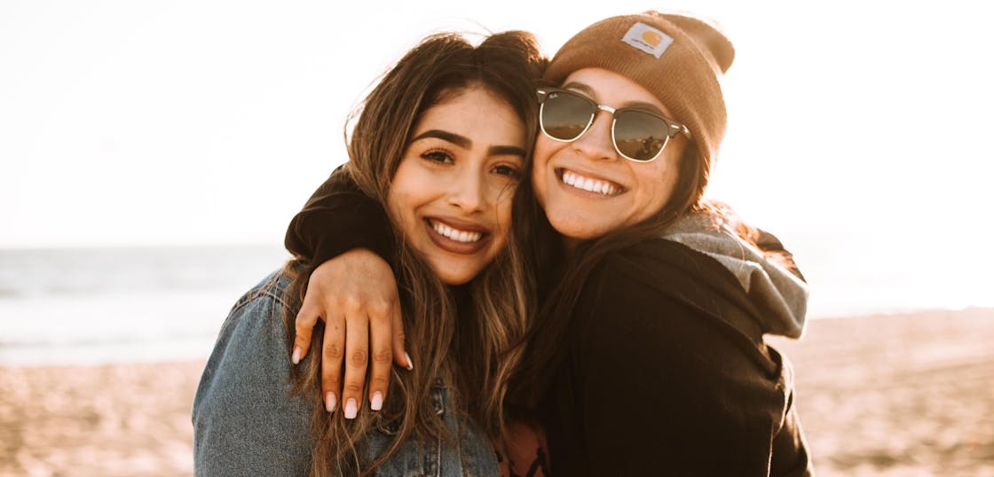 Two women smiling with arms around each other at beach