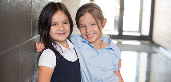 Two young female students standing against wall smiling.