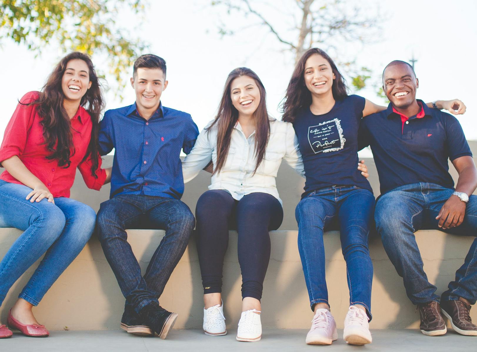 Young adults with arms around each other, smiling, sitting on bench