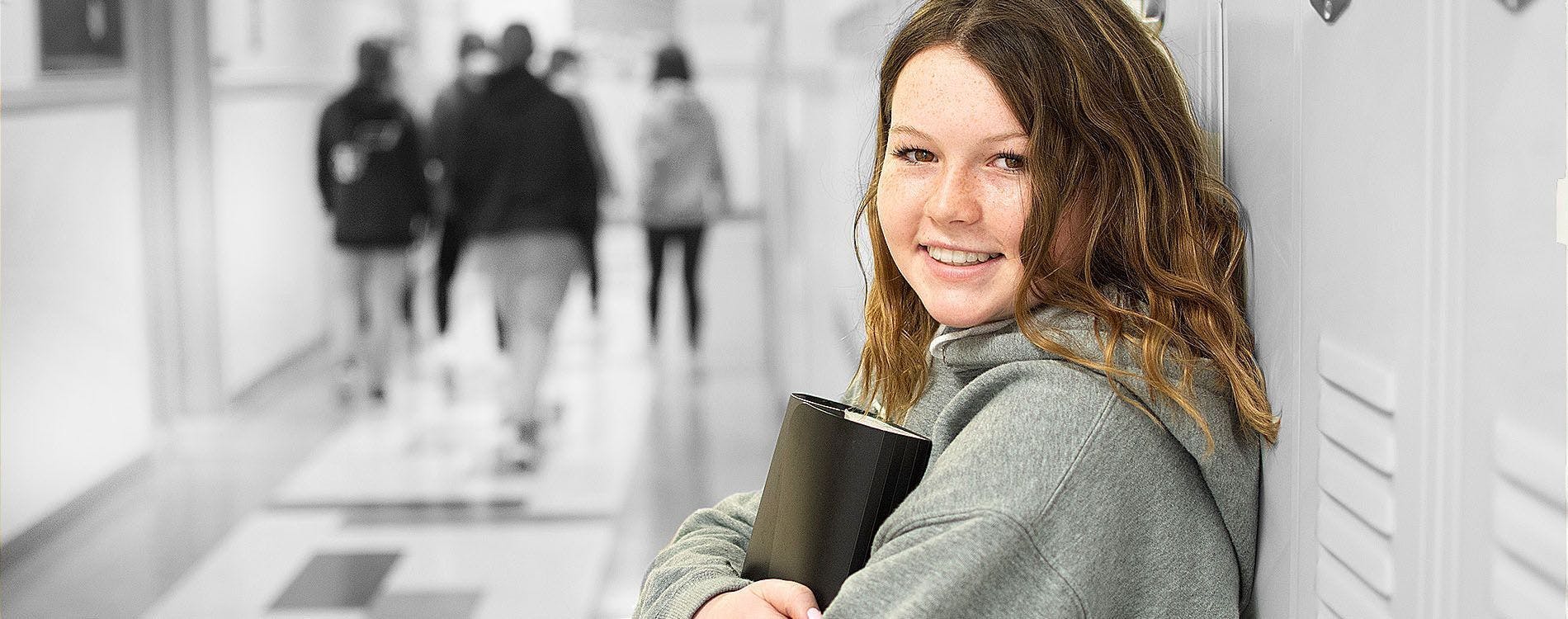 Young female student standing against locker in school hallway